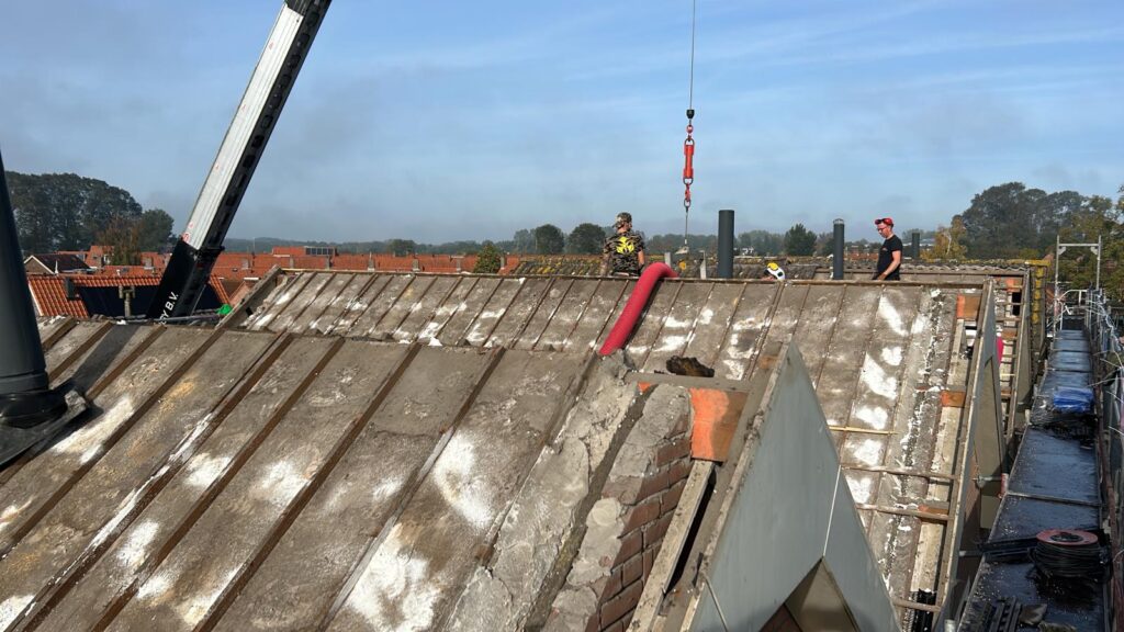 Werkzaamheden op een schuin dak tijdens dakrenovatie met industriële ondersteuning en professionele materiaalafvoer.