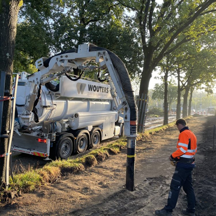 Wouters-zuigwagen met medewerker in bosrijke omgeving tijdens grondwerken en technische ondersteuning op locatie.